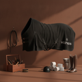 Black horse cooling blanket with Vel de reis branding on a brown background, surrounded by equestrian equipment.