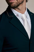 Close-up of a man wearing a dark teal or navy blazer with gold trim, a white dress shirt, and a white tie with a small embroidered monogram.