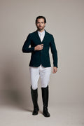 A man modeling a dark teal equestrian blazer, white riding breeches, a white dress shirt, and black riding boots against a neutral beige studio background.