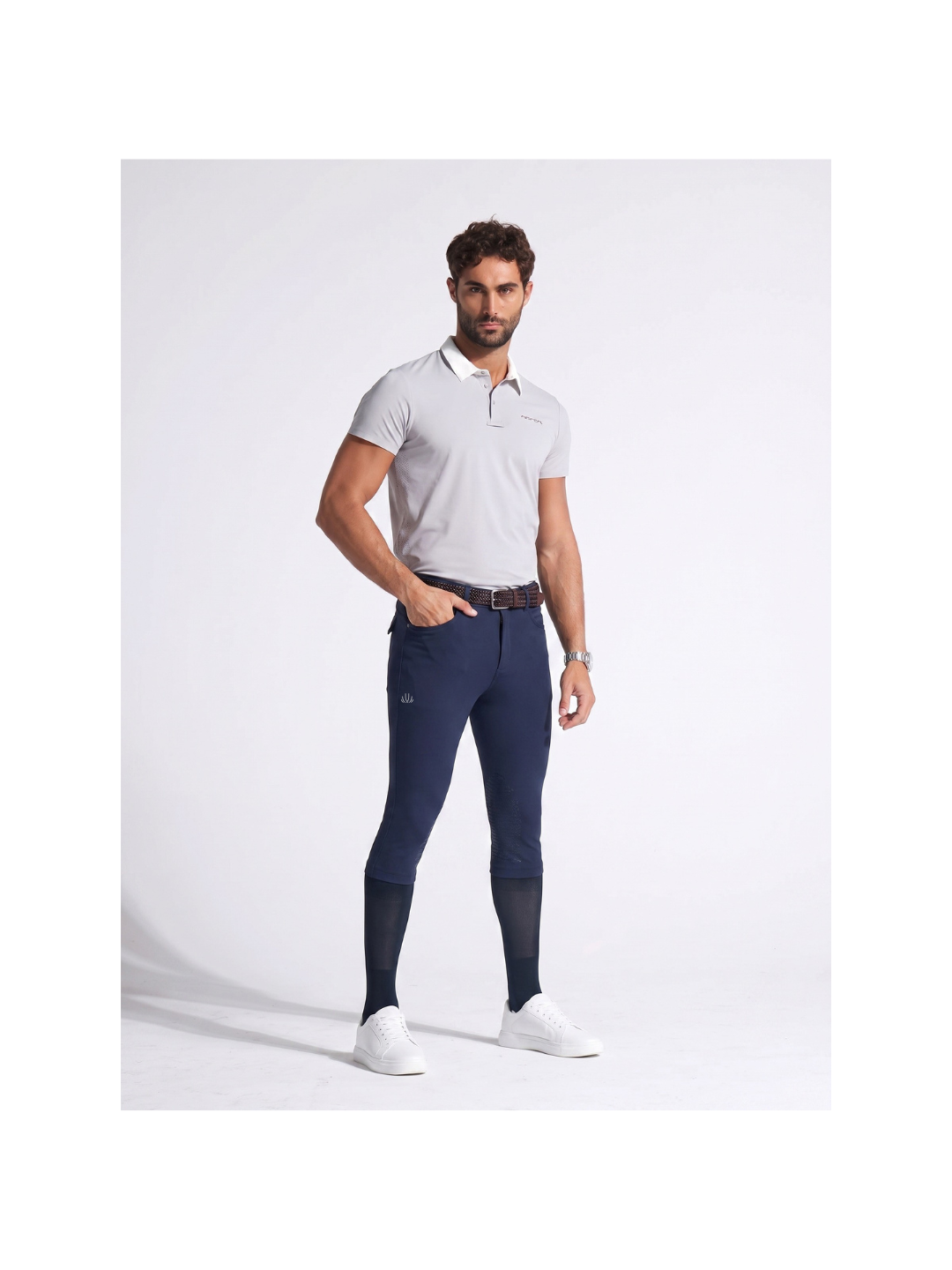 Man wearing a white polo shirt and blue riding pants on a white background