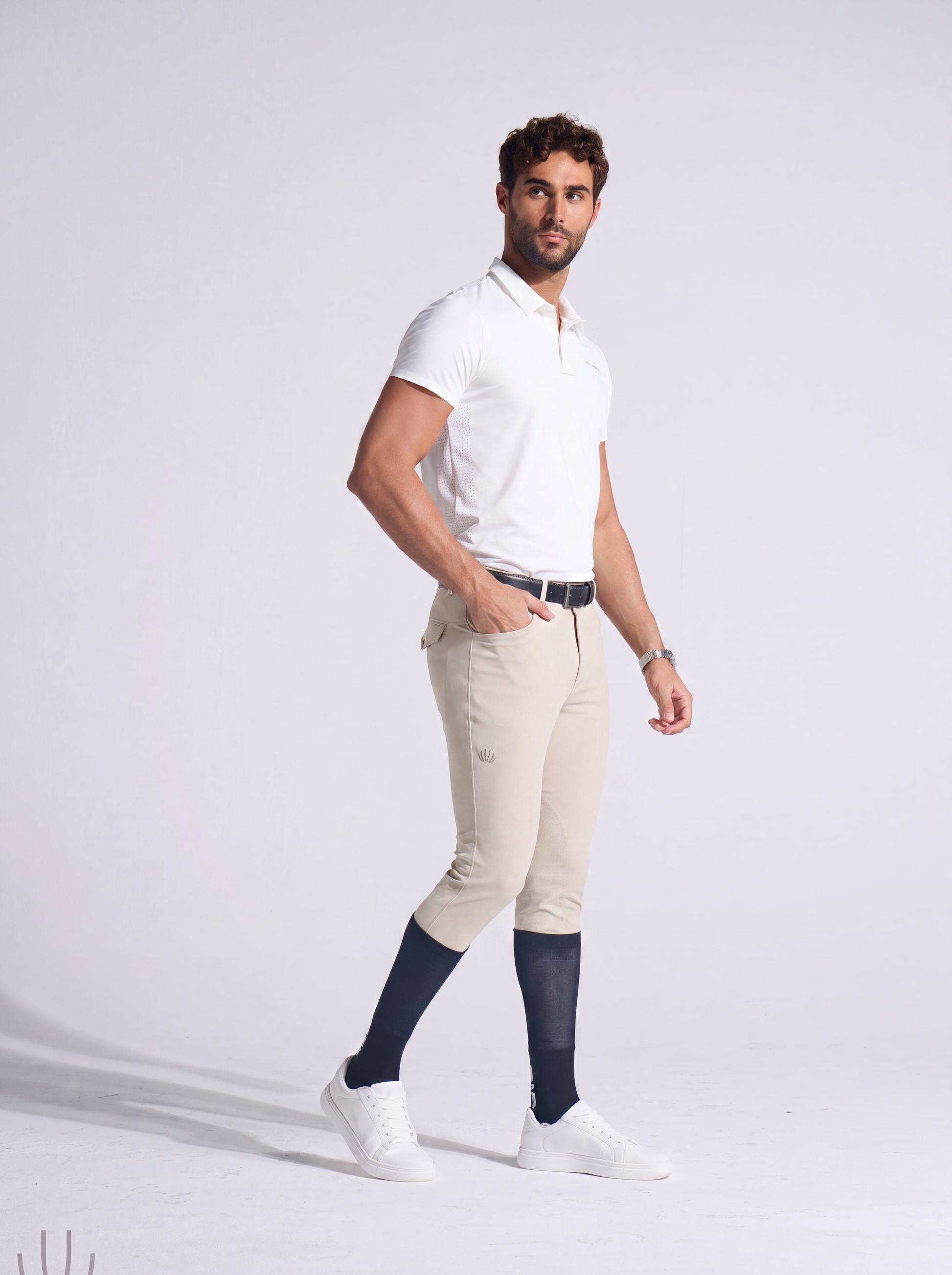 Man wearing a white polo shirt, beige pants, and navy socks on a white background