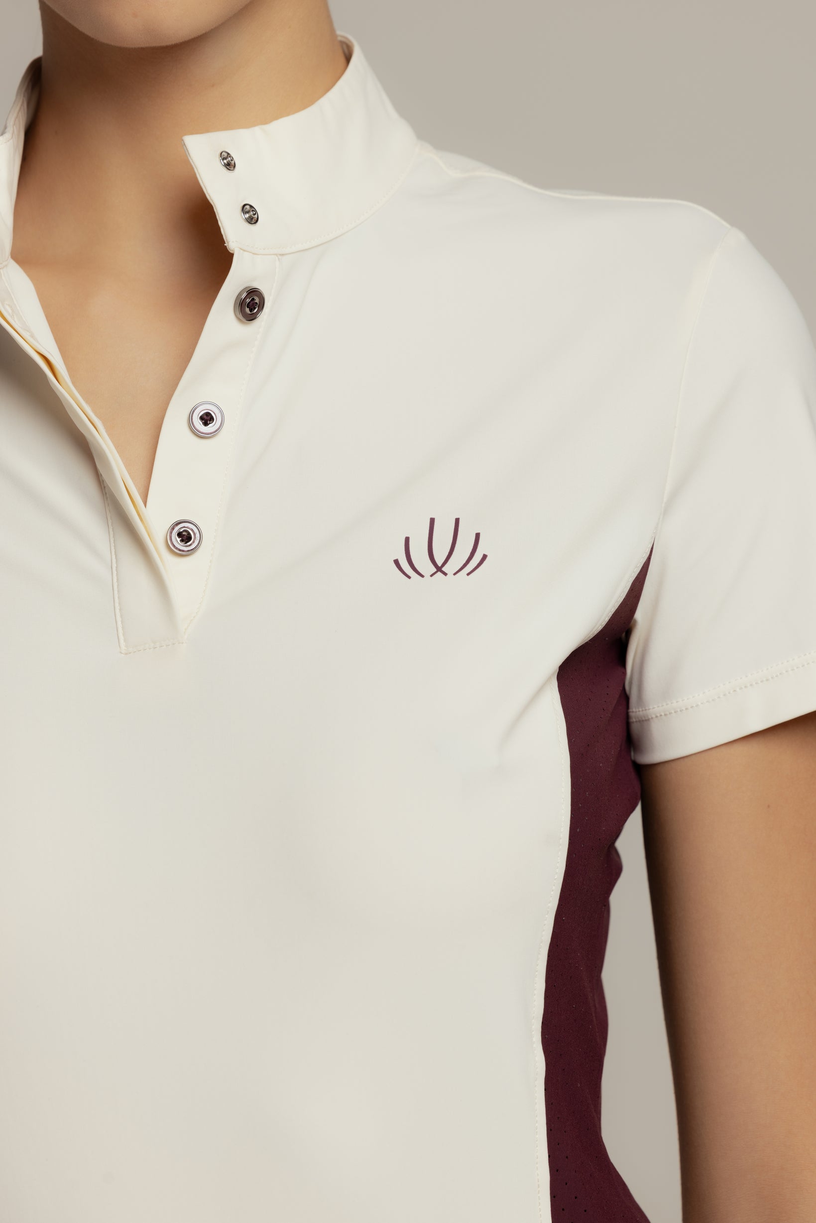 Close-up of a person wearing a short-sleeve polo shirt in off-white with a dark burgundy side panel and matching embroidered chest logo, photographed against a light neutral background.
