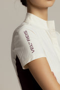 Close-up of a model wearing a white short-sleeve collared shirt with 'VEL D'ESPRIT' printed vertically in dark purple on the upper sleeve, set against a neutral light gray background.