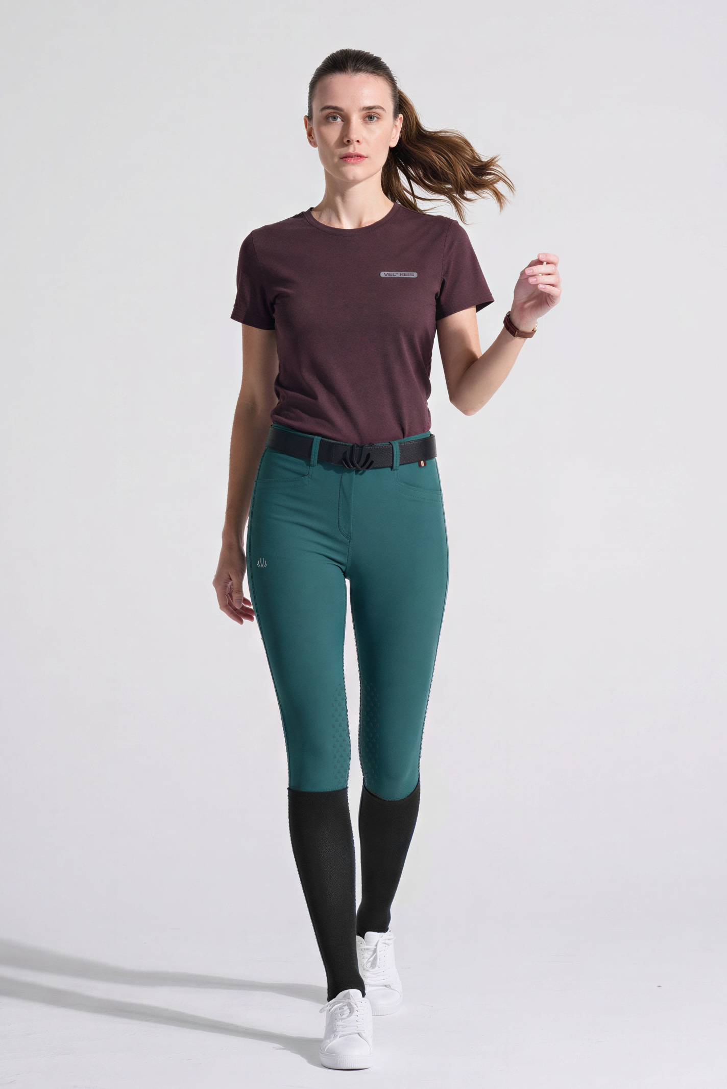 Woman wearing Green riding pants and a Burgundy T-Shirt on a white background