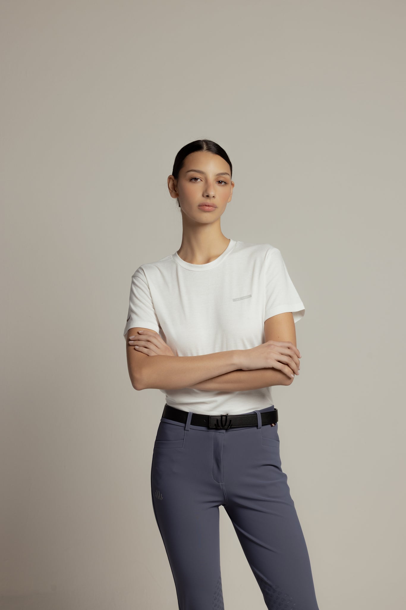A woman modeling a white short-sleeve crewneck t-shirt and slate blue pants against a solid light gray studio background.