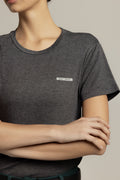 A close-up of a model wearing a dark heather gray crewneck t-shirt with a small white rectangular logo patch on the left chest that reads 'MEL & DUG'.