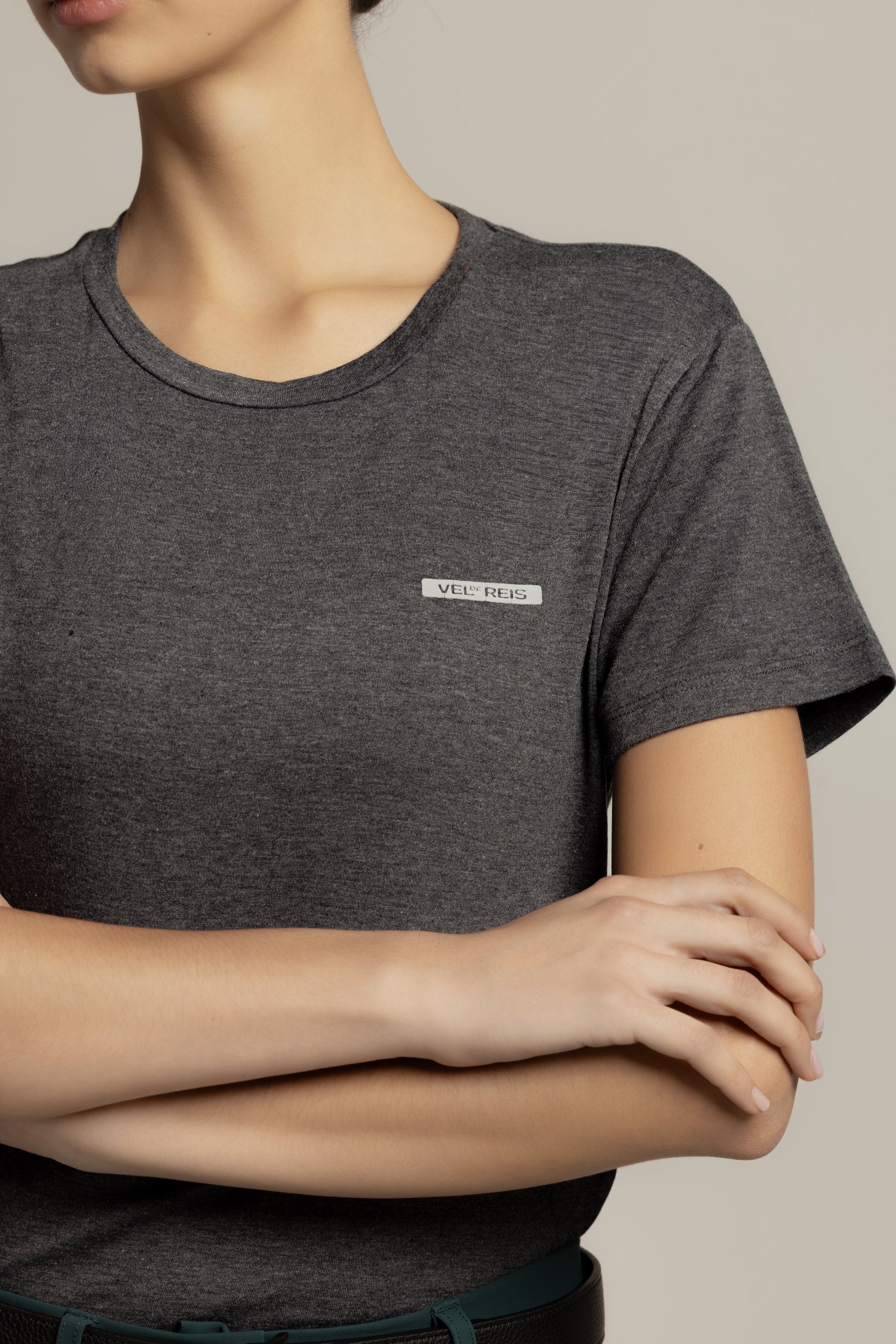 A close-up of a model wearing a dark heather gray crewneck t-shirt with a small white rectangular logo patch on the left chest that reads 'MEL & DUG'.
