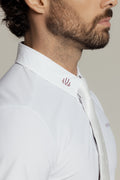 Close-up side profile of a man wearing a white textured dress shirt with a small red embroidered logo on the collar, paired with a white tie against a light gray background.