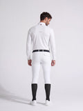 Man wearing a white equestrian suit with black boots on a light gray background
