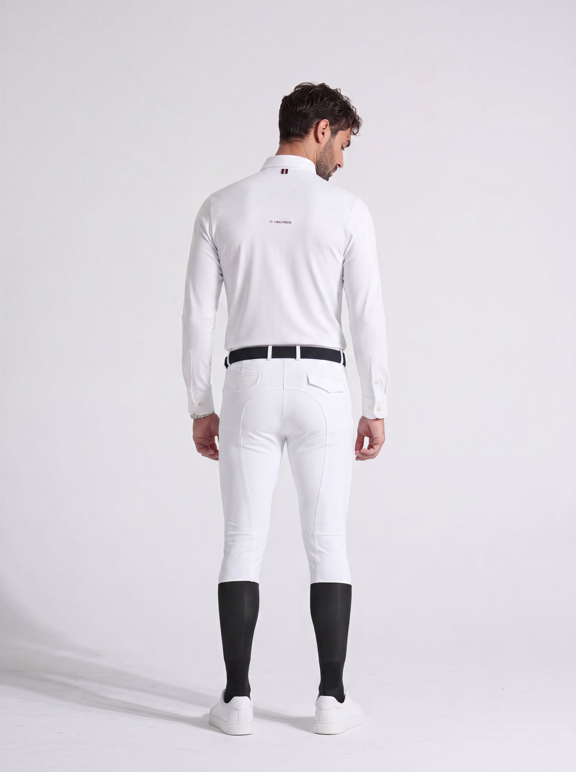 Man wearing a white equestrian suit with black boots on a light gray background
