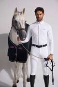 Man in equestrian attire standing next to a horse wearing a black rug.