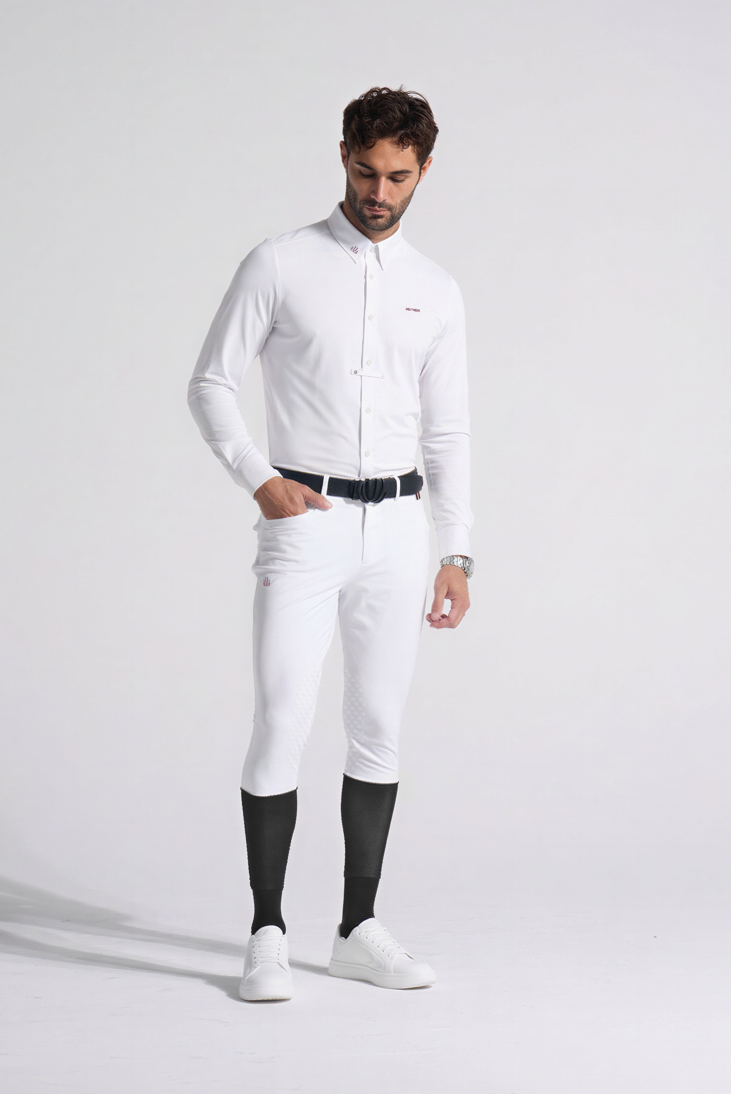 Man wearing a white equestrian outfit with black boots on a plain background