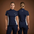 Woman wearing a navy equestrian shirt with white accents, standing against a brown background.