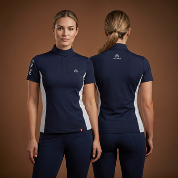 Woman wearing a navy equestrian shirt with white accents, standing against a brown background.