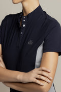 A close-up of a model wearing a dark navy polo shirt with a stand collar, three-button placket, and a small embroidered logo on the left chest. The shirt features light gray color-blocked side panels.