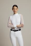 A female model wearing a white high-neck long-sleeve riding shirt with sheer sleeves, paired with white riding pants and a black belt, against a solid light gray studio background.