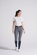 Woman wearing gray riding pants and a white shirt on a white background