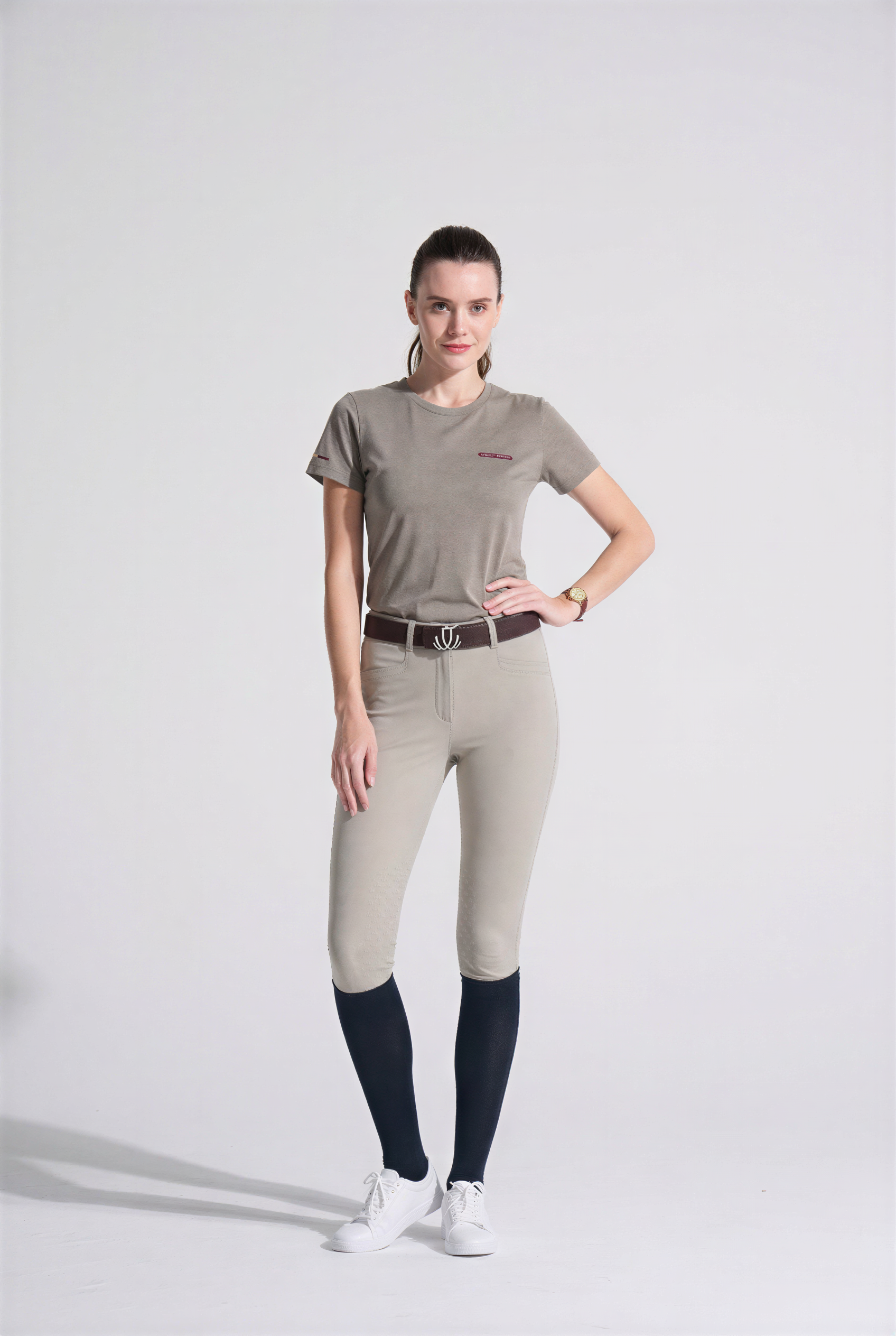 Woman wearing beige riding pants and a matching VEL DE REIS T-Shirt on a white background