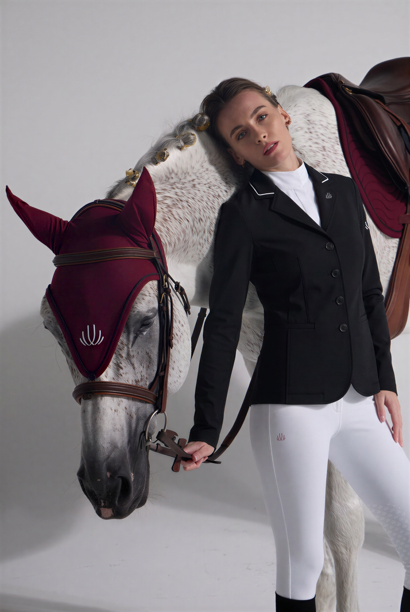 Woman in VEL DE REIS equestrian Clothes standing next to a horse with a red hood.