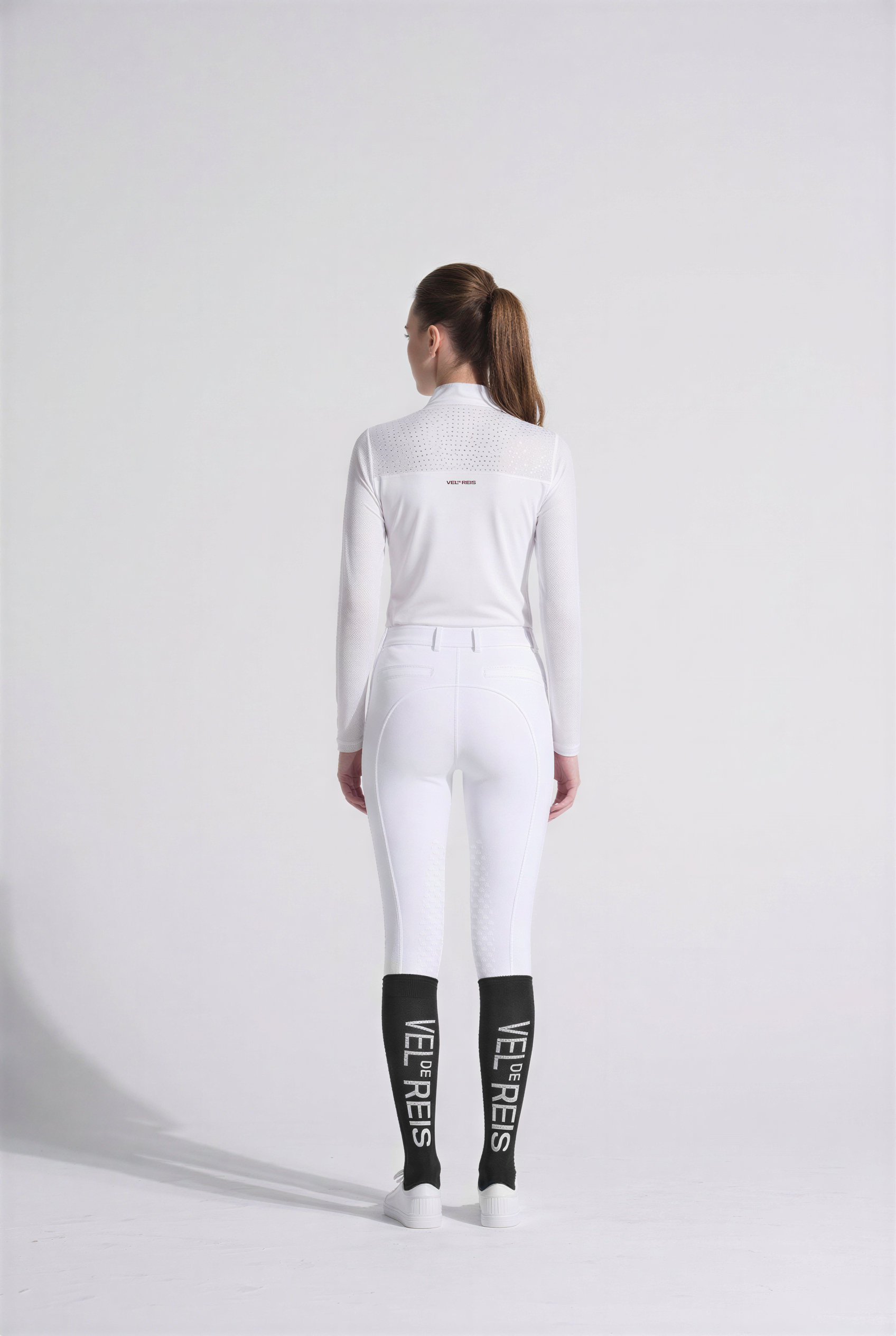Women rider wearing a white VEL DE REIS equestrian outfit with black boots on a white background