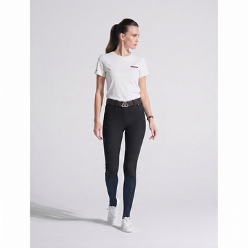 Woman wearing black riding pants and a white shirt on a light gray background