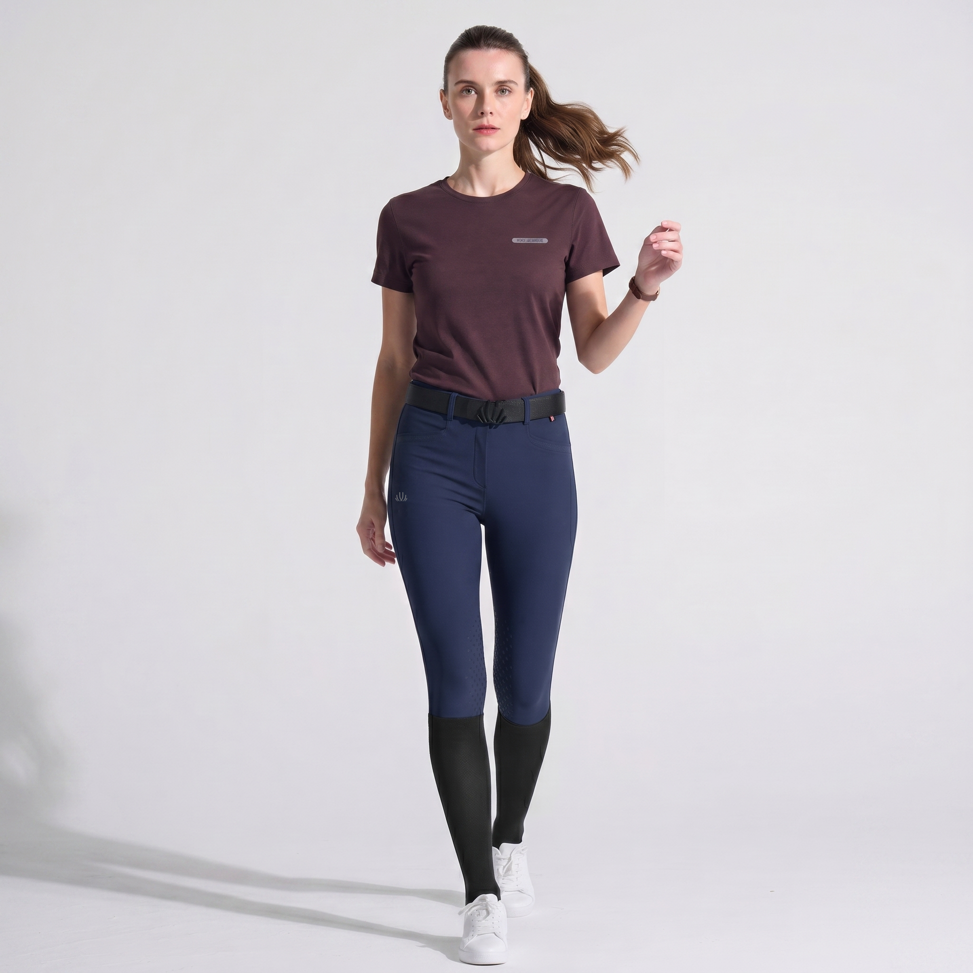 Woman wearing a maroon shirt and dark blue riding pants on a white background