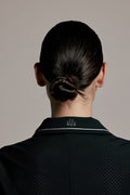 Back view of a person with dark hair in a low bun, wearing a black collared shirt with a small white embroidered logo on the collar, against a plain light gray background.