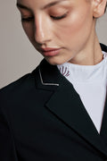 Close-up of a model wearing a black structured blazer with white contrast piping over a white mock-neck top, against a neutral beige background.