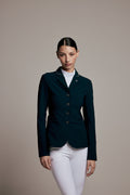 A woman modeling a dark navy equestrian blazer with white pants, standing against a solid beige studio background.