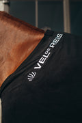 Horse wearing a black blanket with 'VELDE REIS' branding on a dark background